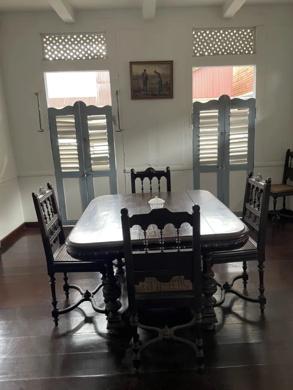 Salle à manger avec table en bois précieux, chaises sculptées et persiennes bleues